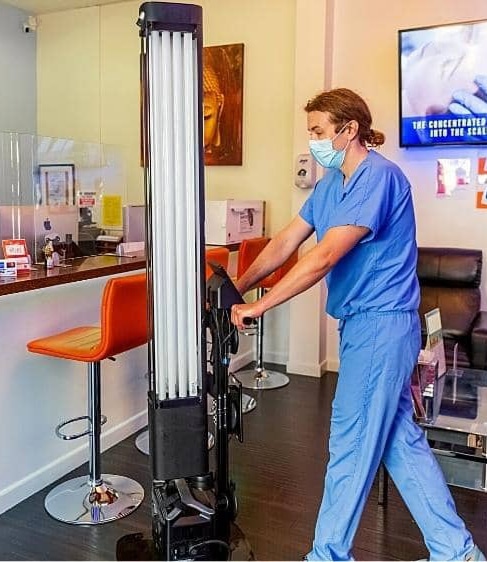 A person in scrubs pushing the UV-C disinfection robot from OhmniLabs.