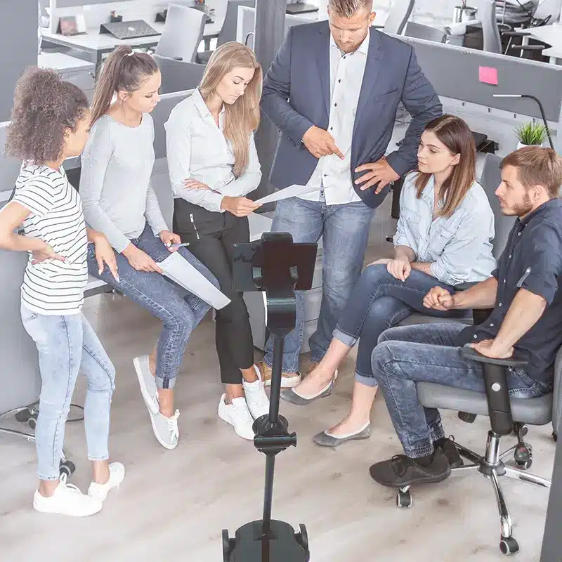 A group of employees holding a meeting with a meeting robot present.
